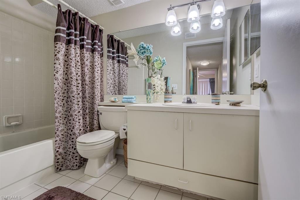 Full bath with shower / tub combo with curtain, light tile patterned floors, vanity, and a textured ceiling