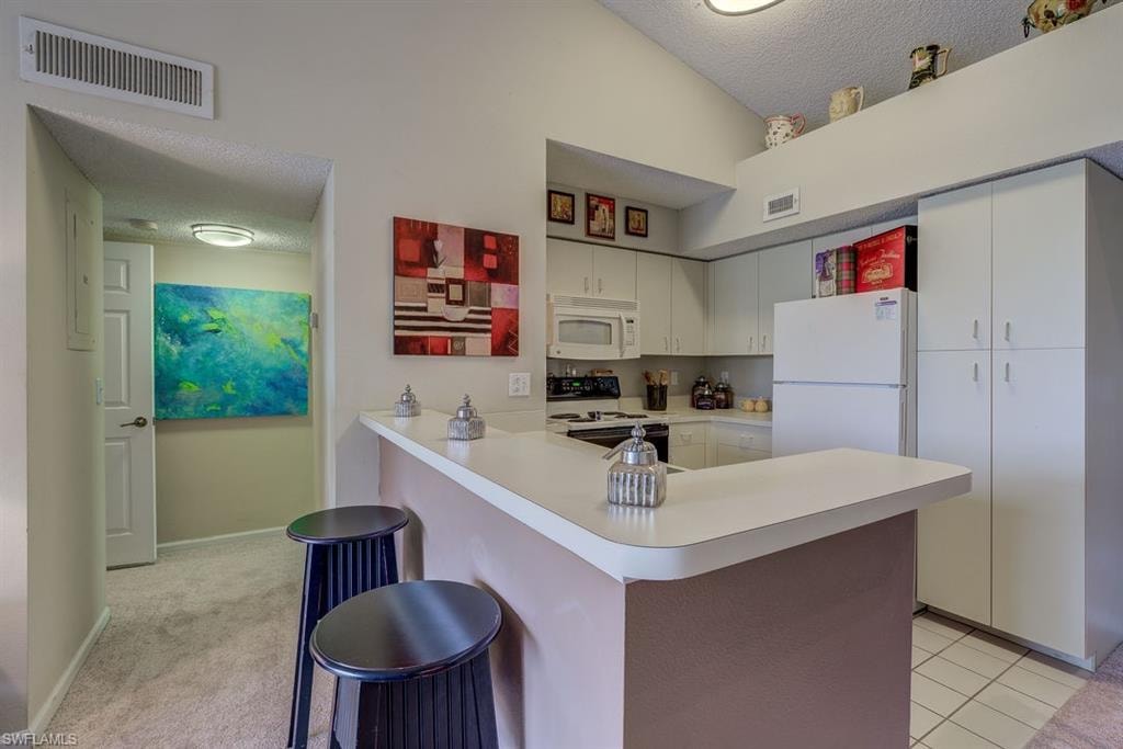 Kitchen with a textured ceiling, a breakfast bar, light countertops, white appliances, and white cabinetry