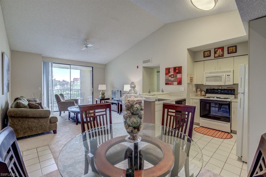 Dining room with vaulted ceiling, light tile patterned floors, a textured ceiling, and ceiling fan