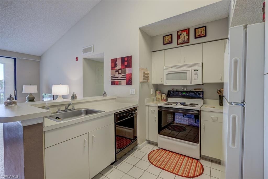 Kitchen with white appliances, a peninsula, white cabinets, a textured ceiling, and light tile patterned floors
