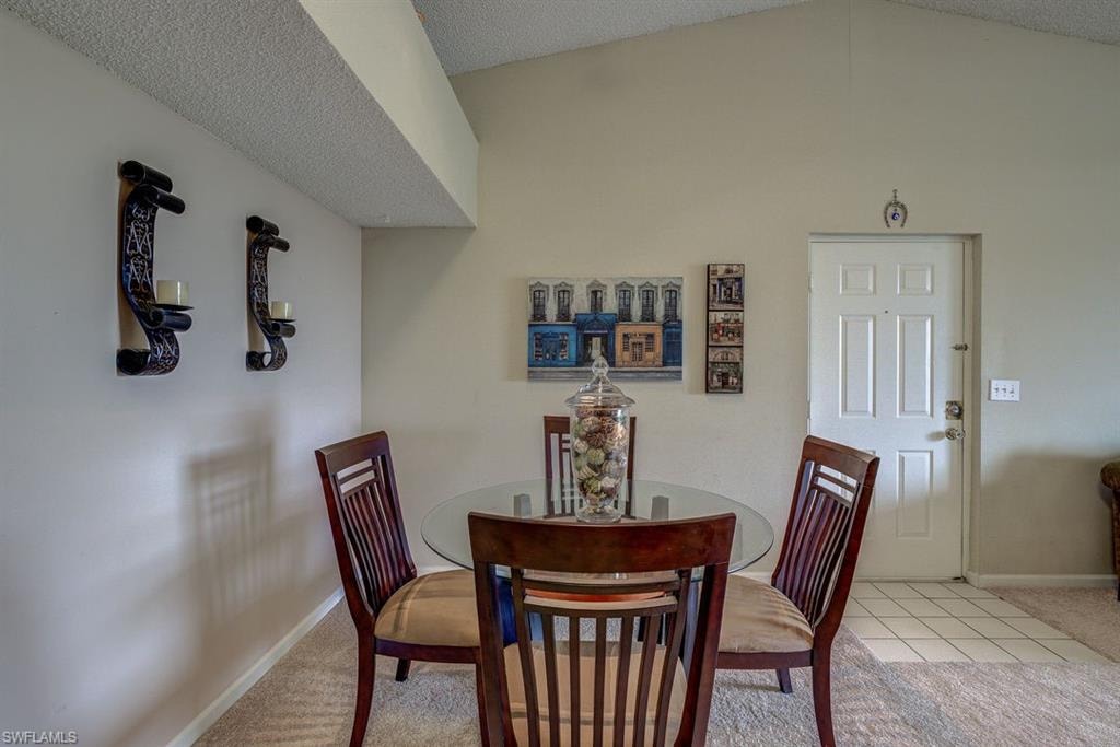 Dining area with carpet, lofted ceiling, tile patterned floors, and a textured ceiling