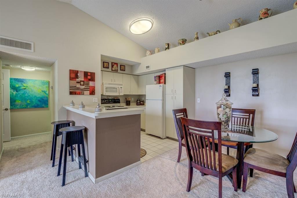 Kitchen with light countertops, a kitchen breakfast bar, white appliances, lofted ceiling, and a peninsula