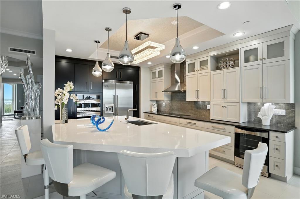 Kitchen with decorative light fixtures, light tile patterned flooring, decorative backsplash, wine cooler, and appliances with stainless steel finishes - Virtually Edited Image