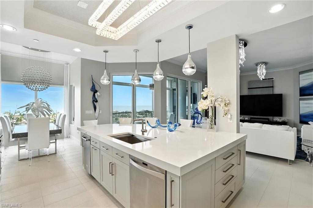 Kitchen featuring crown molding, a chandelier, a tray ceiling, pendant lighting, and stainless steel dishwasher - Virtually Edited Image
