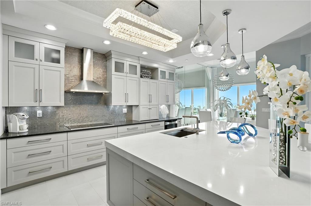 Kitchen with wall chimney range hood, glass insert cabinets, gray cabinetry, pendant lighting, and recessed lighting - Virtually Edited Image
