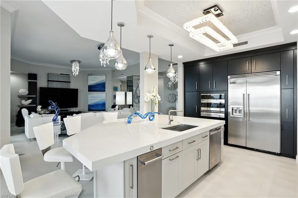 Kitchen featuring ornamental molding, a raised ceiling, a breakfast bar, stainless steel appliances, and decorative light fixtures - Virtually Edited Image