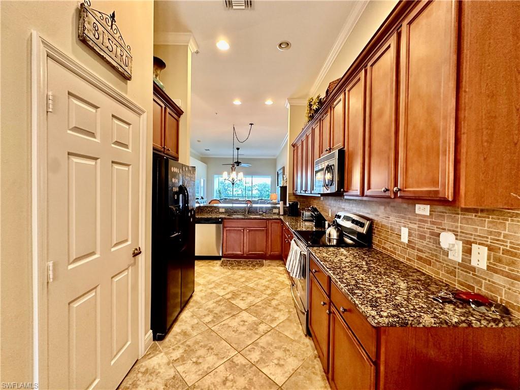 Kitchen featuring dark stone countertops, appliances with stainless steel finishes, light tile patterned flooring, ceiling fan, and ornamental molding