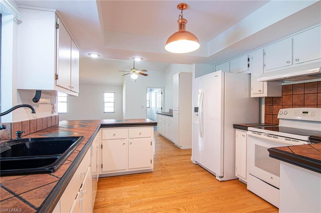 Kitchen with white range with electric cooktop, a peninsula, hanging light fixtures, light wood-style flooring, and under cabinet range hood