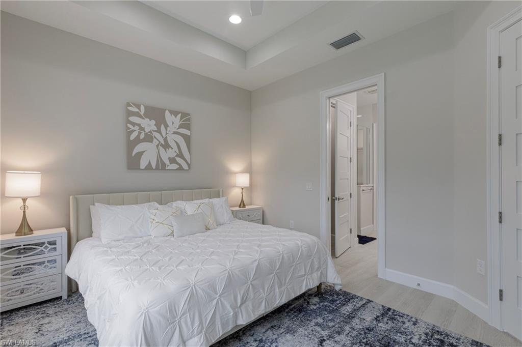 Bedroom featuring light wood finished floors, recessed lighting, ensuite bath, a ceiling fan, and a raised ceiling