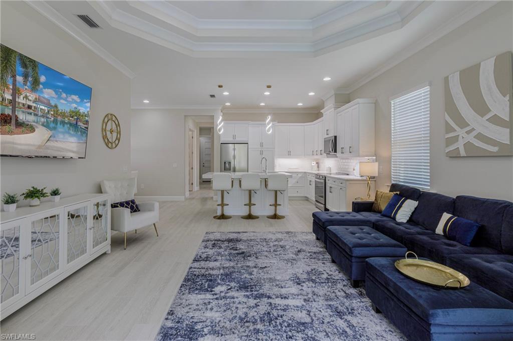 Living area with ornamental molding, a tray ceiling, light wood-style floors, and recessed lighting