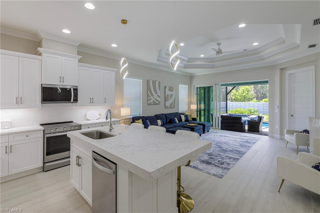 Kitchen with open floor plan, white cabinetry, stainless steel appliances, a center island with sink, and recessed lighting