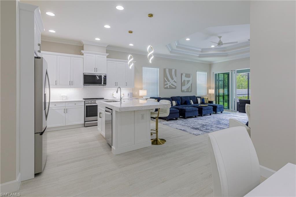 Kitchen with open floor plan, decorative backsplash, white cabinetry, an island with sink, and pendant lighting