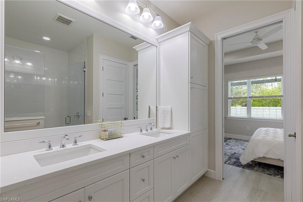 Full bathroom with a shower stall, double vanity, ceiling fan, and light wood-style flooring