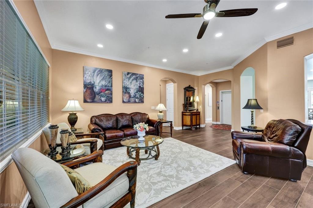 Living room with ornamental molding, dark wood-style floors, arched walkways, recessed lighting, and a ceiling fan