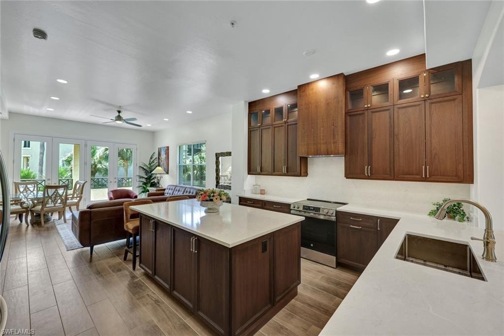 Kitchen featuring a kitchen island, stainless steel electric stove, glass insert cabinets, a ceiling fan, and dark wood-type flooring