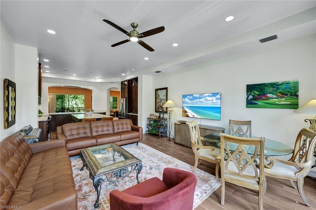 Living room featuring light wood-type flooring, arched walkways, recessed lighting, and ceiling fan