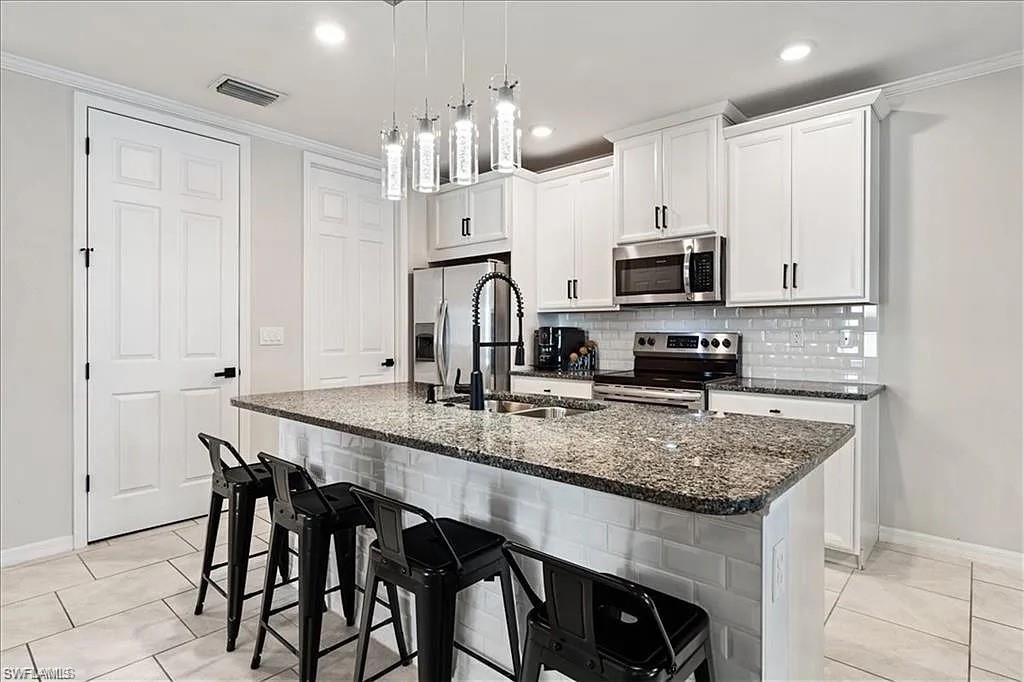 Kitchen featuring ornamental molding, dark stone countertops, a breakfast bar, stainless steel appliances, and white cabinetry