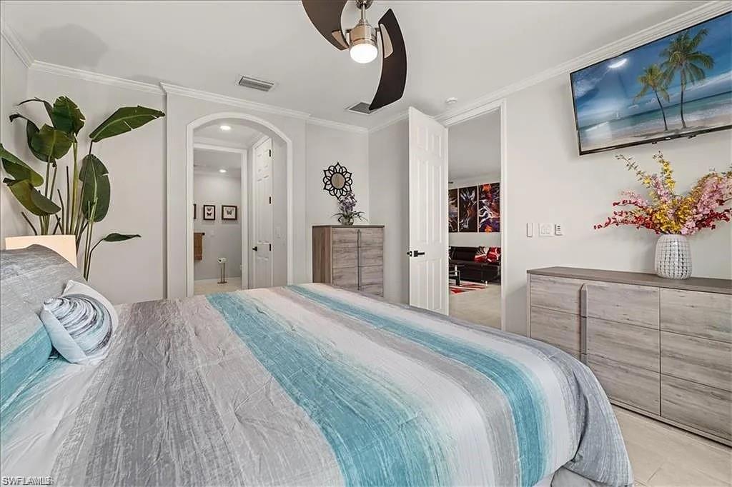 Bedroom with ornamental molding, a ceiling fan, connected bathroom, and arched walkways
