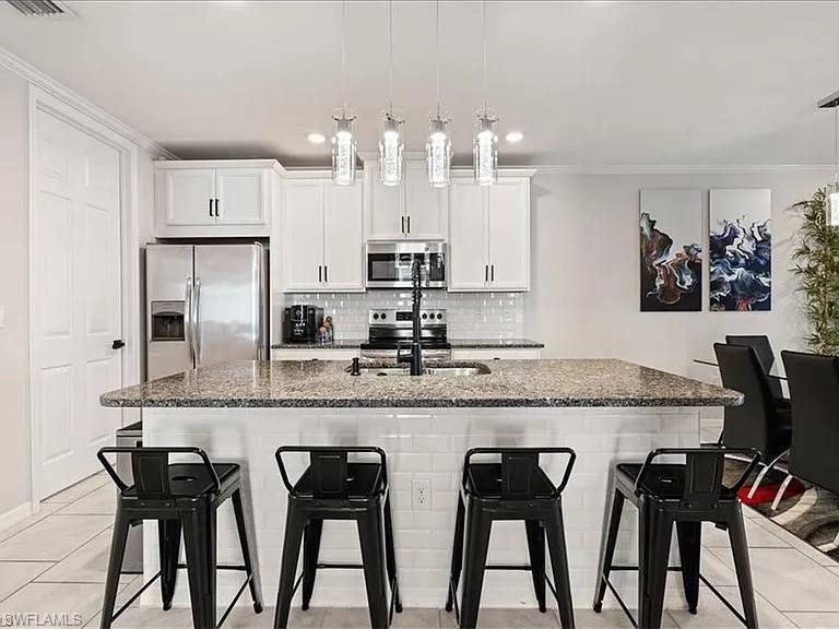 Kitchen featuring light tile patterned floors, appliances with stainless steel finishes, ornamental molding, a kitchen breakfast bar, and decorative backsplash