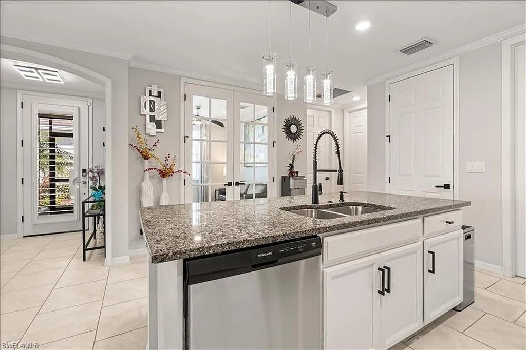 Kitchen featuring french doors, stainless steel dishwasher, light tile patterned floors, pendant lighting, and white cabinets