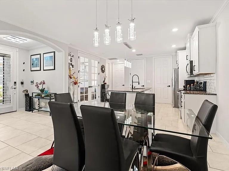 Dining space with light tile patterned flooring, french doors, crown molding, arched walkways, and recessed lighting