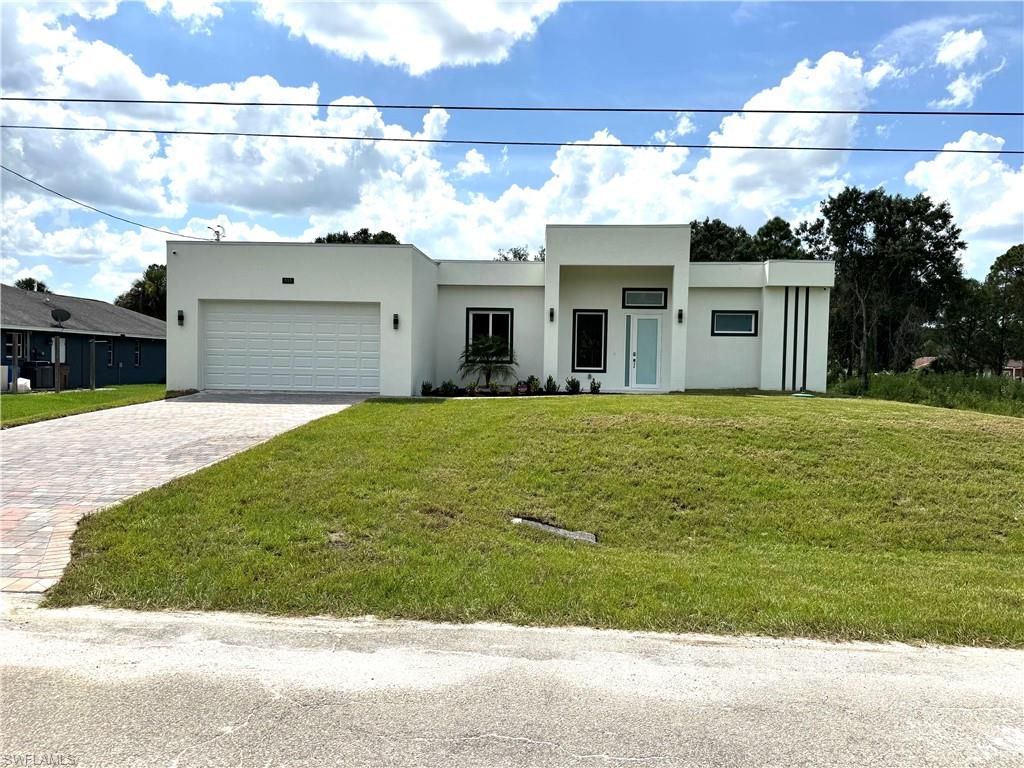 Contemporary house featuring a front lawn, stucco siding, decorative driveway, and an attached garage