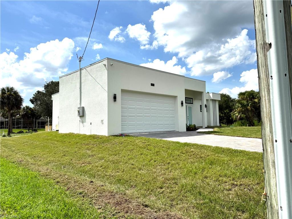 Modern home featuring stucco siding, a front lawn, a garage, and driveway