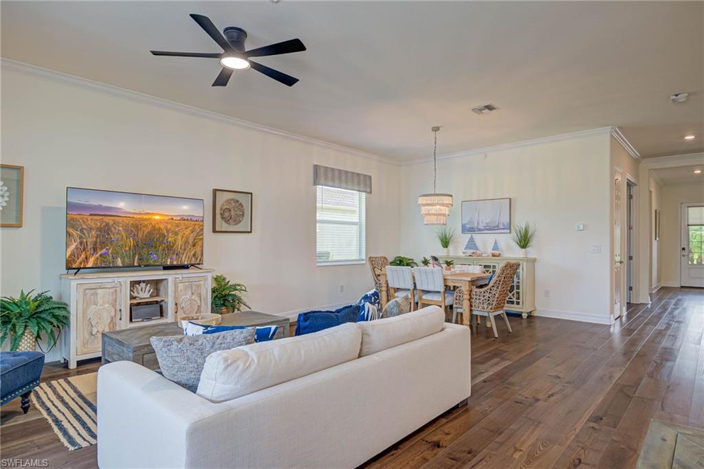 Living room with ornamental molding, dark wood-style flooring, plenty of natural light, and a ceiling fan