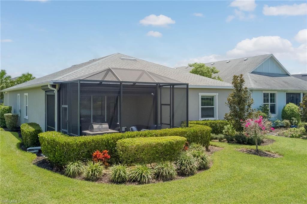 Back of house with a shingled roof, a yard, a lanai, stucco siding, and a sunroom