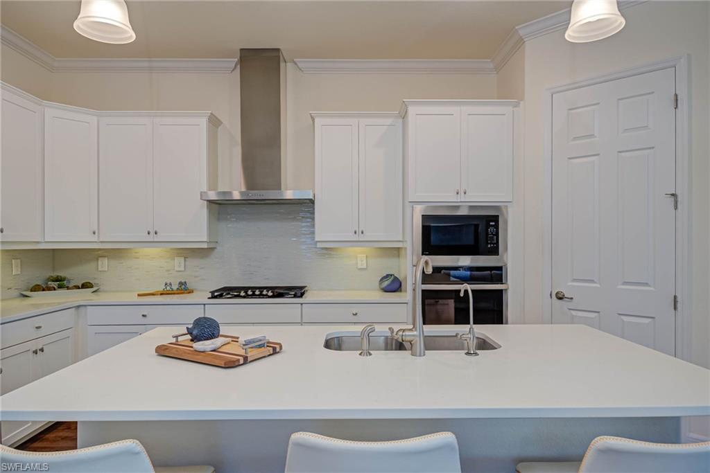 Kitchen featuring tasteful backsplash, a kitchen breakfast bar, wall chimney exhaust hood, crown molding, and white cabinets