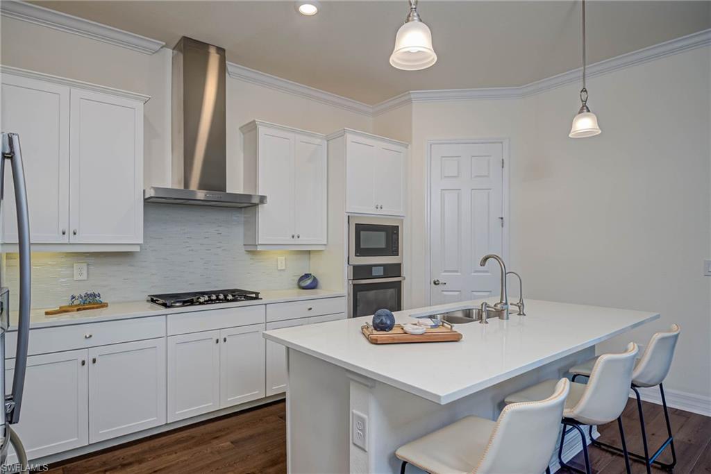 Kitchen with decorative backsplash, a breakfast bar area, dark wood-style flooring, white cabinetry, and ornamental molding