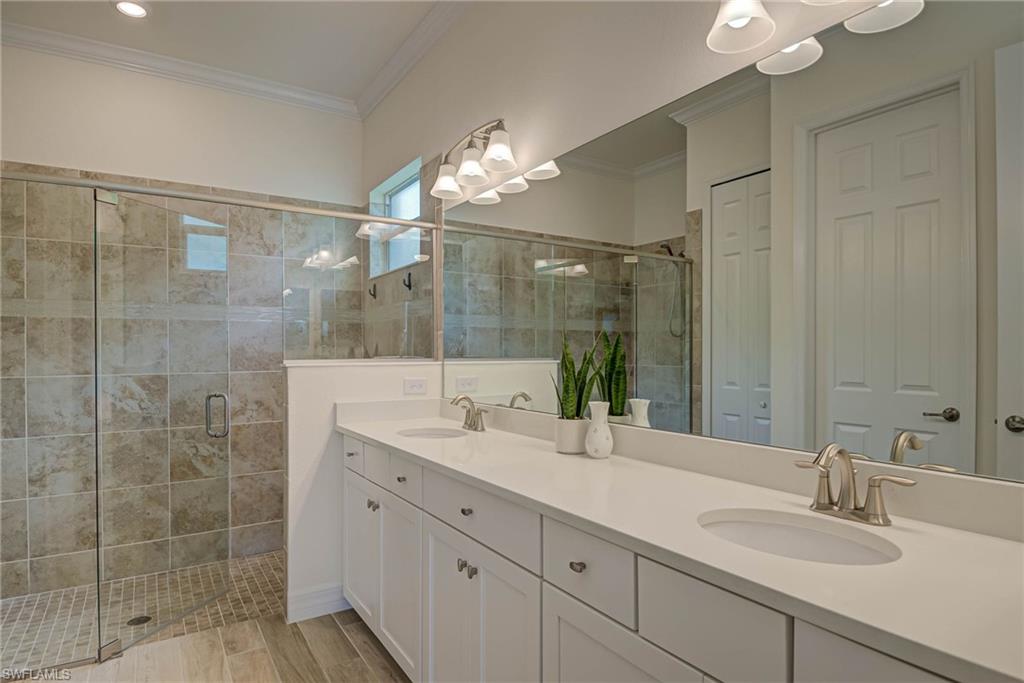 Bathroom with a shower stall, double vanity, ornamental molding, and a closet