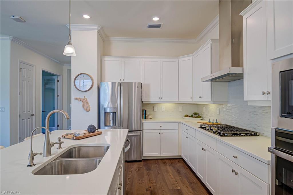 Kitchen featuring ornamental molding, white cabinets, appliances with stainless steel finishes, decorative backsplash, and dark wood-style floors