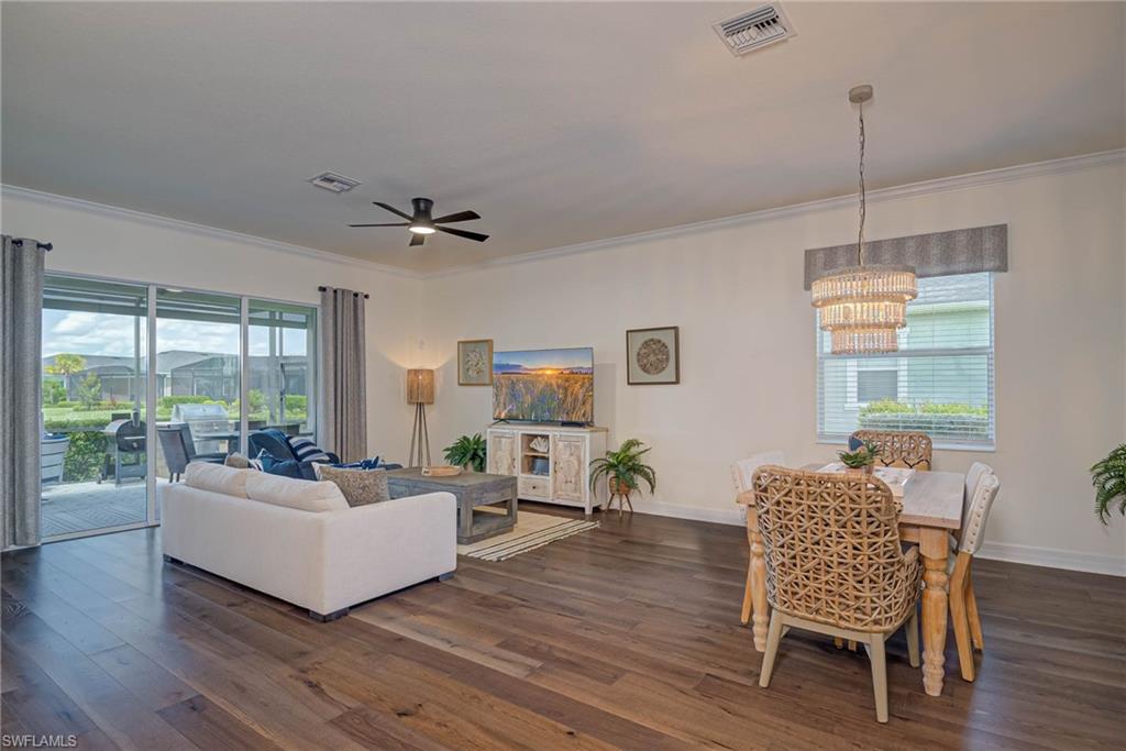 Living room with dark wood-style flooring, crown molding, a ceiling fan, and a chandelier