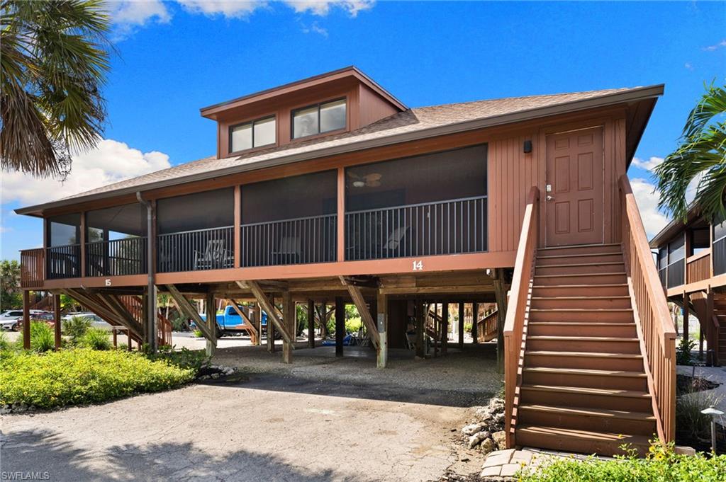 View of front of house with dirt driveway, stairway, a carport, roof with shingles, and a sunroom