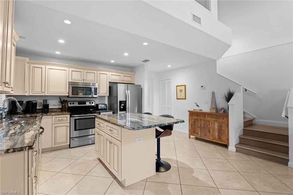 Kitchen featuring cream cabinets, dark stone countertops, stainless steel appliances, a kitchen bar, and recessed lighting