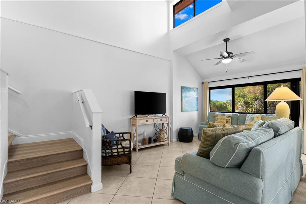 Living area featuring high vaulted ceiling, healthy amount of natural light, light tile patterned floors, a ceiling fan, and stairs