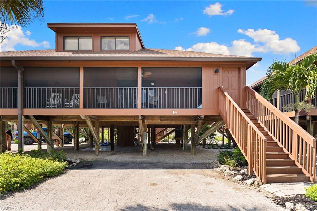 Coastal home with a carport, dirt driveway, a shingled roof, a deck, and stairway