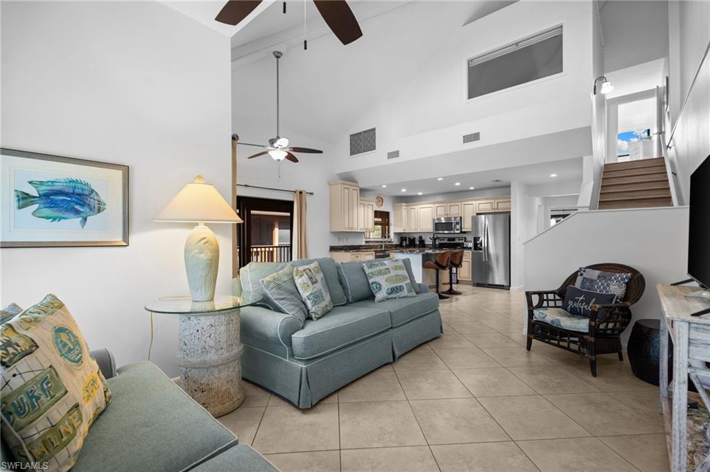 Living room with stairs, light tile patterned floors, high vaulted ceiling, and ceiling fan