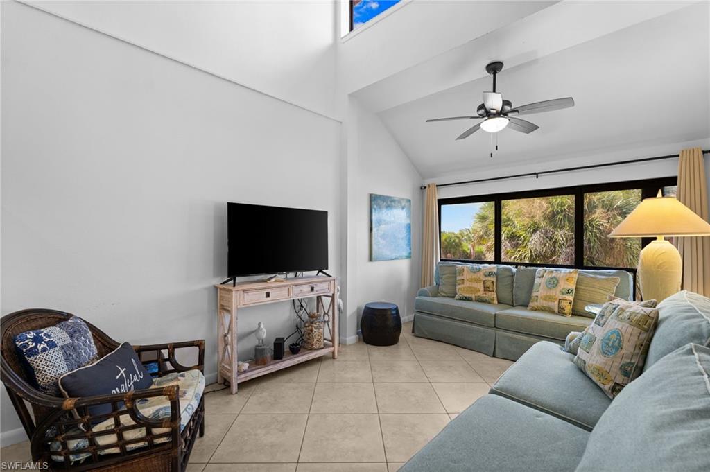 Living room with healthy amount of natural light, light tile patterned floors, high vaulted ceiling, and a ceiling fan