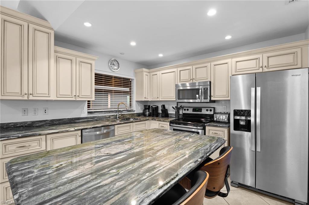 Kitchen with cream cabinets, dark stone countertops, stainless steel appliances, light tile patterned flooring, and recessed lighting