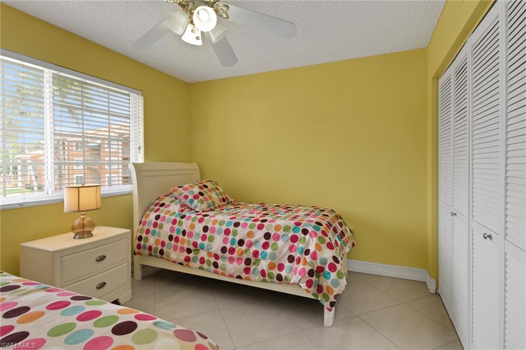 Bedroom with light tile patterned floors, a closet, a textured ceiling, and a ceiling fan
