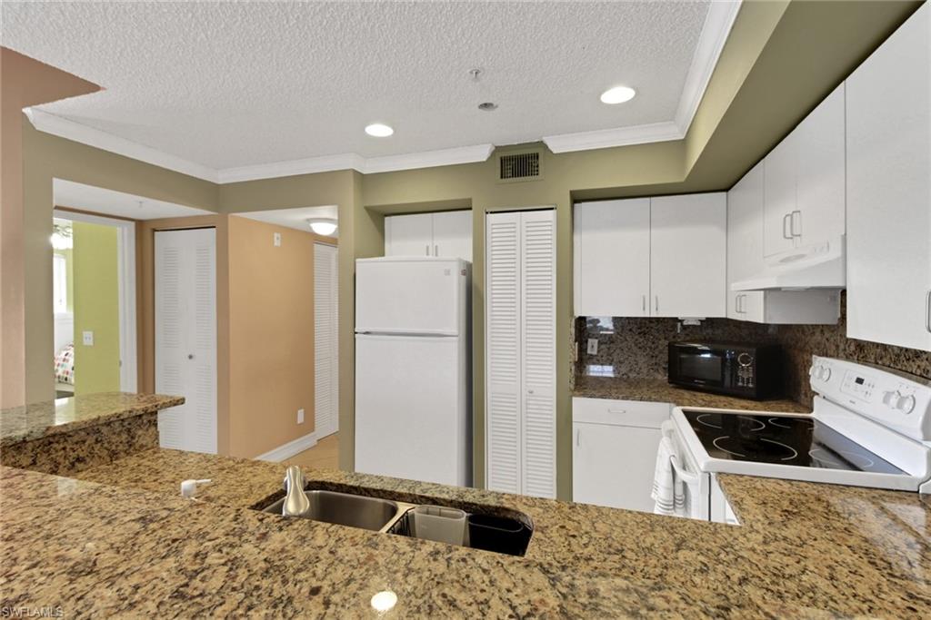 Kitchen with ornamental molding, white appliances, white cabinetry, a textured ceiling, and decorative backsplash
