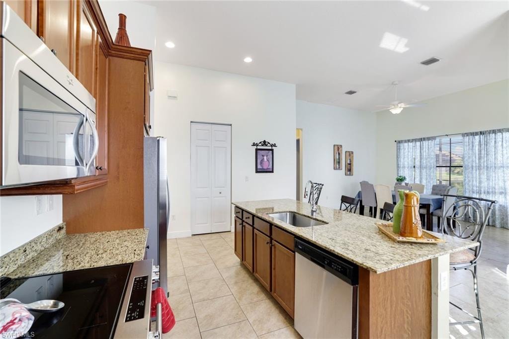 Kitchen featuring brown cabinetry, light stone counters, stainless steel appliances, light tile patterned flooring, and recessed lighting
