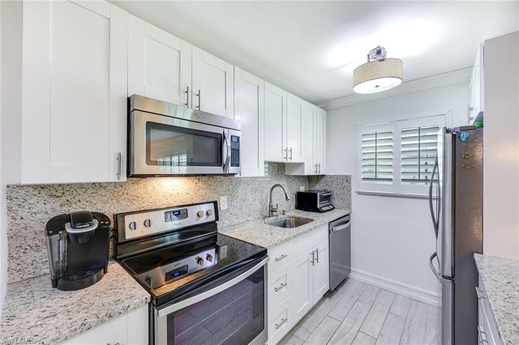 Kitchen with appliances with stainless steel finishes, white cabinets, light stone countertops, and crown molding