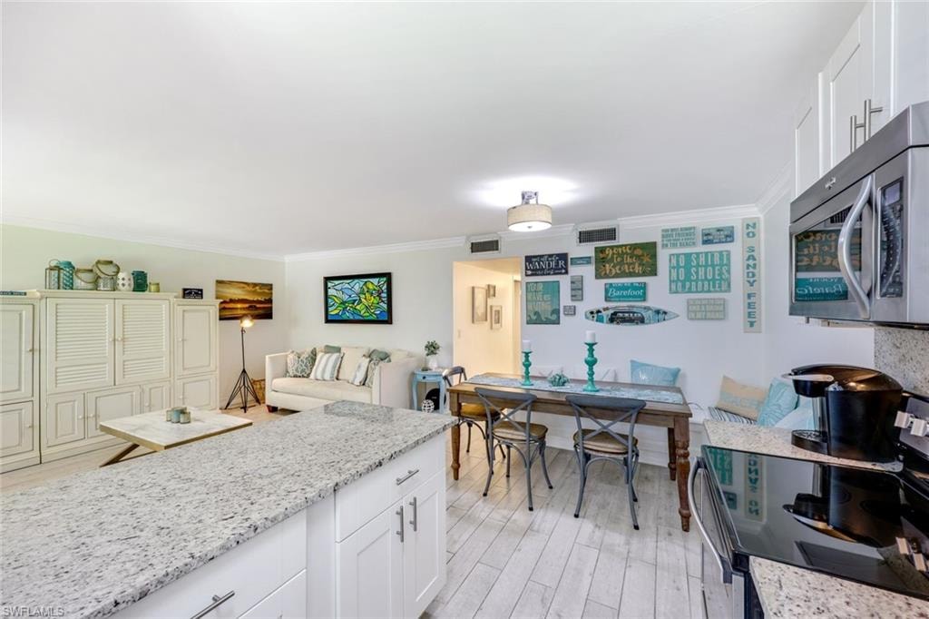 Kitchen with white cabinets, electric range, light stone counters, stainless steel microwave, and crown molding