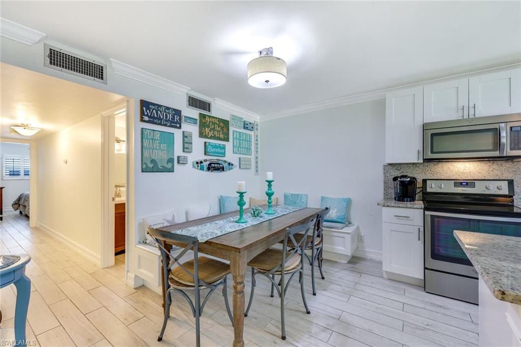 Kitchen with appliances with stainless steel finishes, ornamental molding, backsplash, light wood-style floors, and white cabinets
