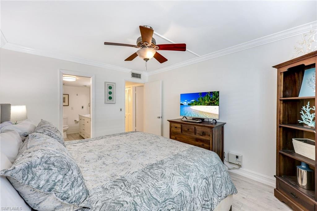 Bedroom with light wood-type flooring, crown molding, ceiling fan, and ensuite bath