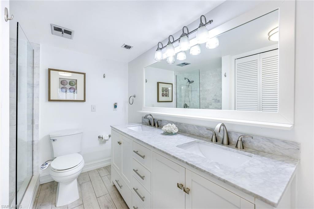 Bathroom with double vanity, a stall shower, wood finish floors, and a closet