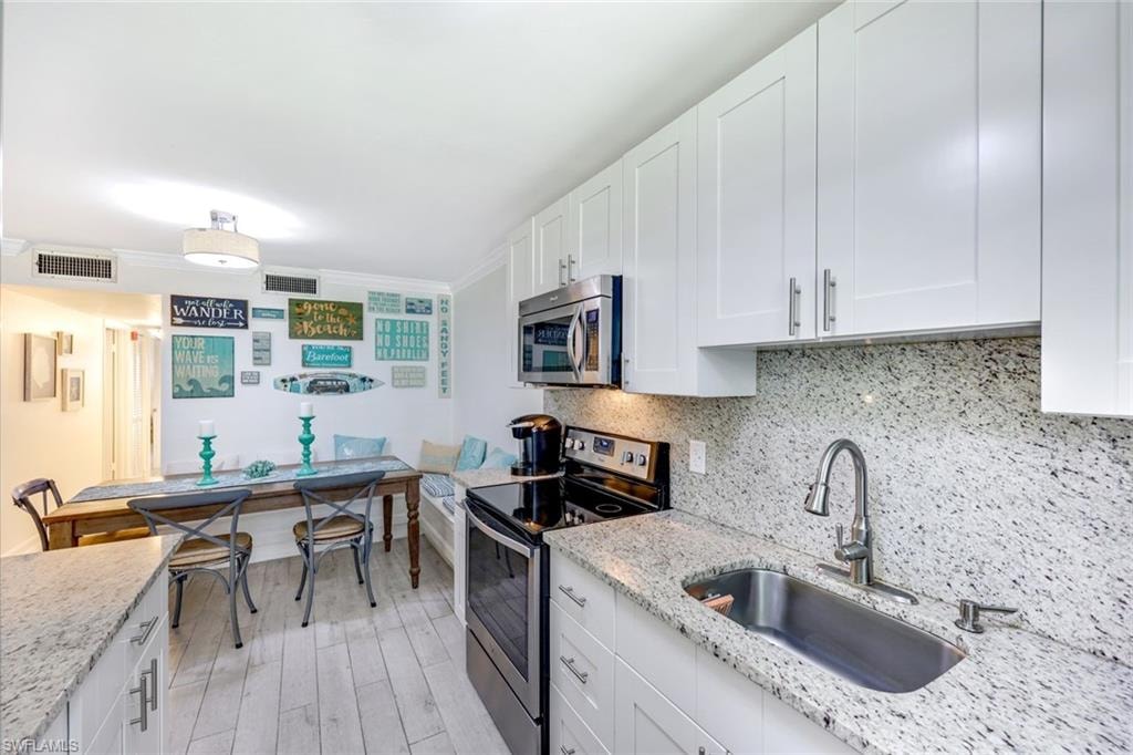 Kitchen featuring stainless steel appliances, tasteful backsplash, white cabinets, crown molding, and light wood-style flooring